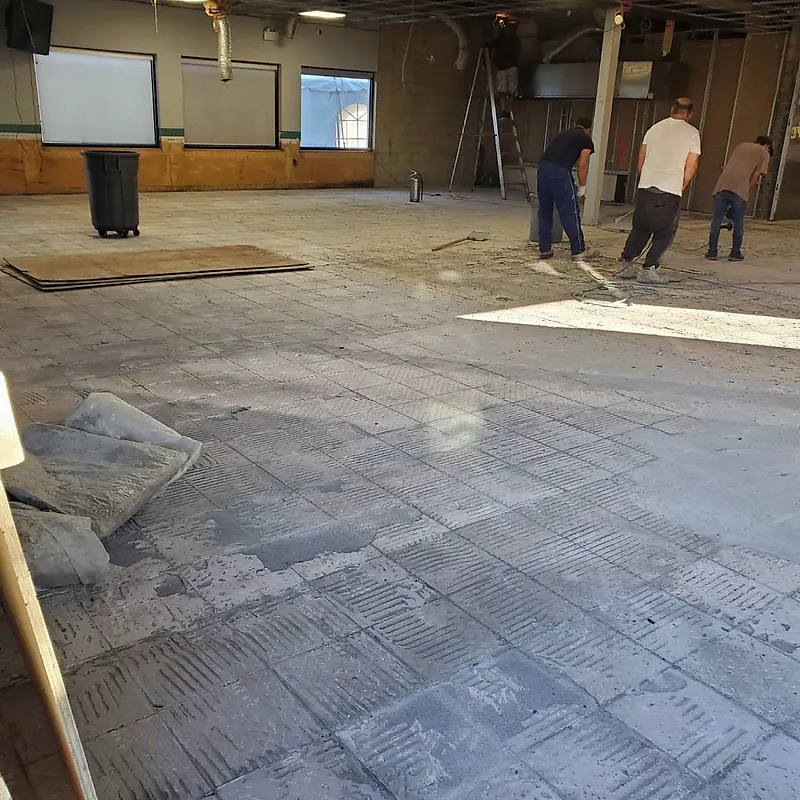 Three workers scraping a dining room floor with most of the tile already removed