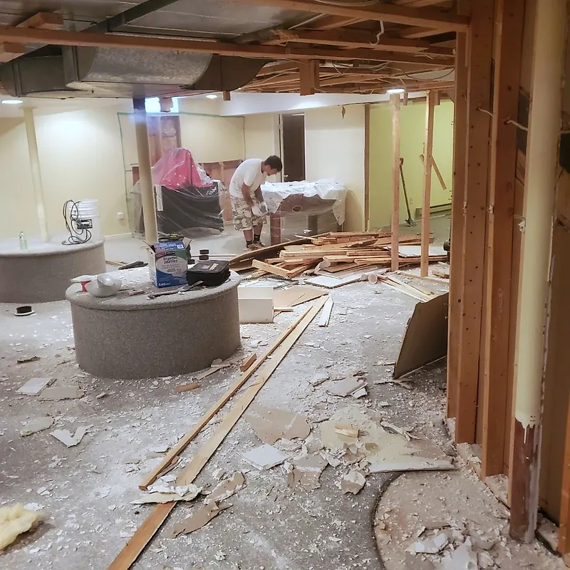 Worker clearing a basement rec room, boards and broken drywall on the floor