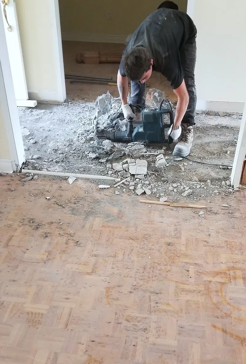 Worker breaking out a mortar bed with an electric breaker next to a parquet floor