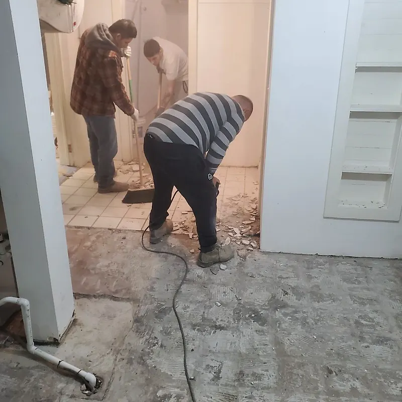 Three workers taking up tile in a bathroom doorway, one with a breaker