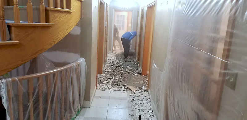 Hallway lined with plastic sheeting from floor to ceiling while tile is broken up at the far end