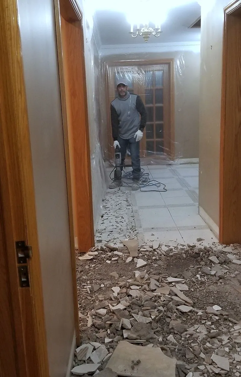 Long hallway with broken tile piled on the floor and a worker at the far end