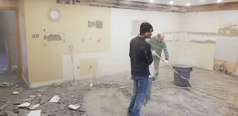 Kitchen with the cabinets already removed and broken floor tile being cleared