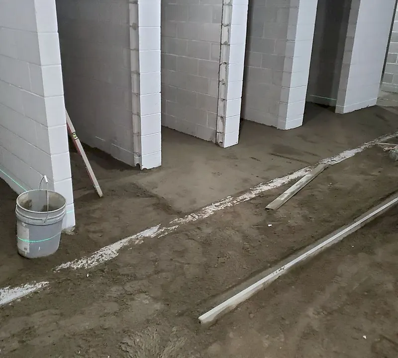 Block-walled cubicle area with loose and part-screeded mortar, a chalk line, straightedges and laser lines on the walls