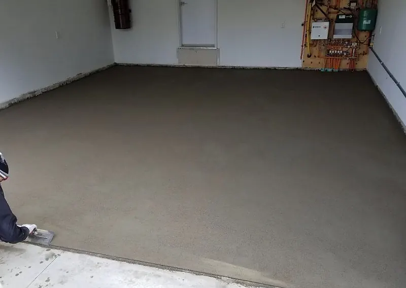 Two-car garage with a fresh, even mortar floor bed and a worker floating the edge