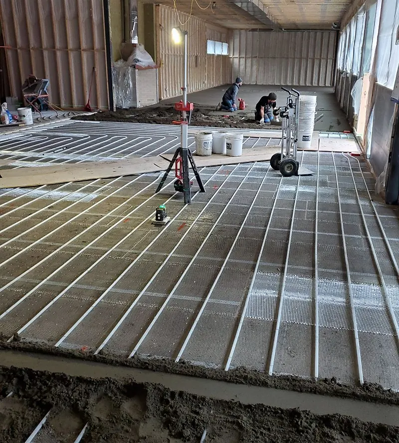 Heating tubes on mesh with a laser on a tripod and a screeded band of mortar in the foreground