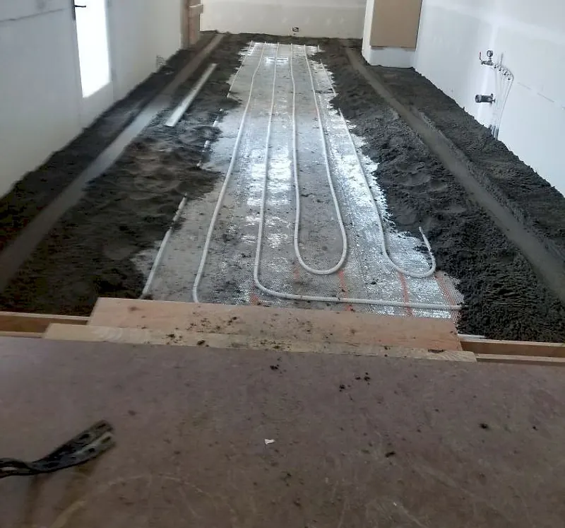 Room in a house with heating loops on a reflective underlay and dark mortar spread along both sides between screed rails