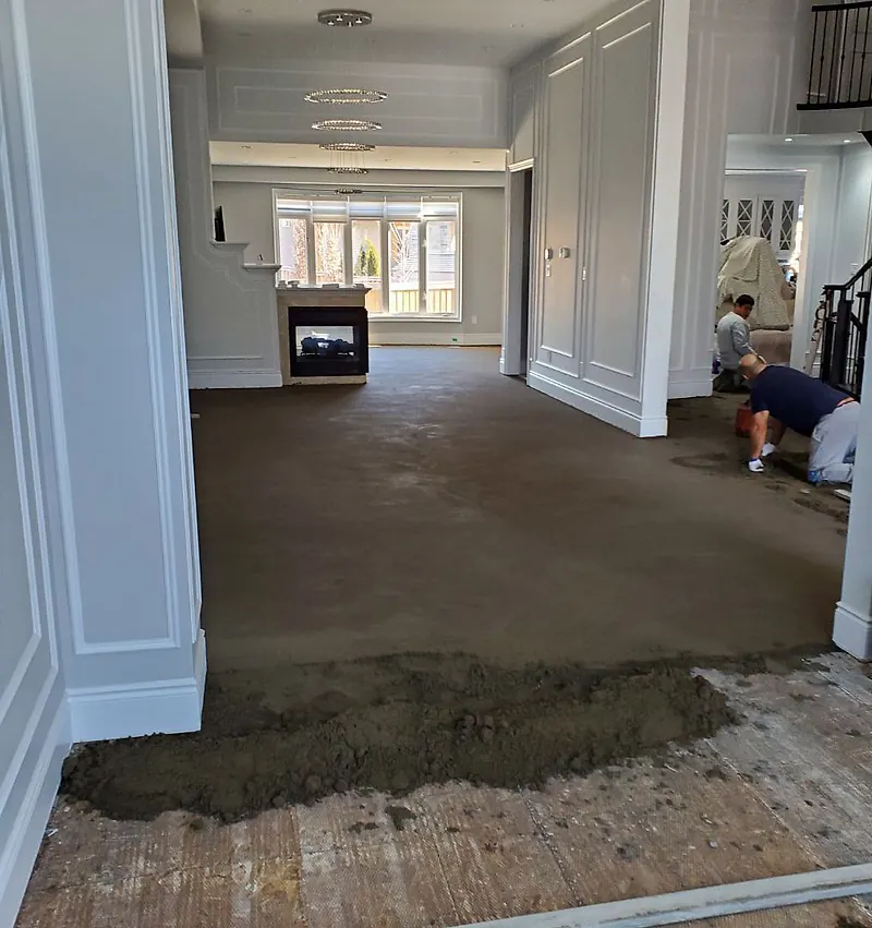 Panelled living room with a fireplace and chandeliers, a large smooth dry pack floor screed and two workers kneeling at the far side