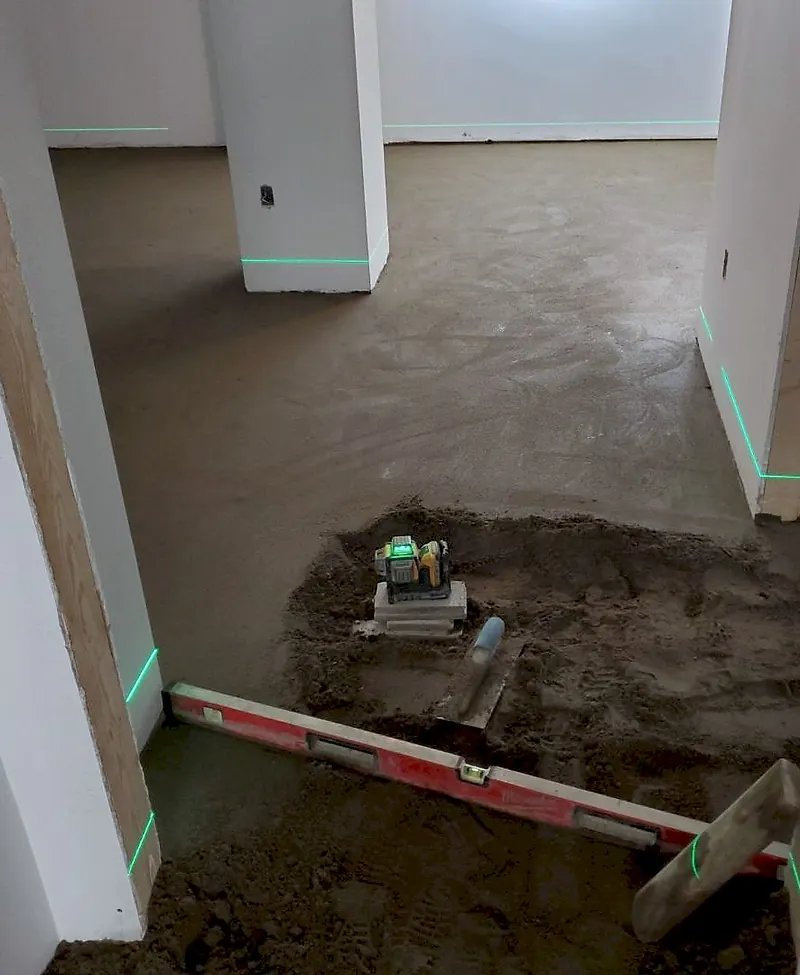 Green laser lines on walls and door frames, a laser level on a block over loose mortar, a level and a float in the doorway