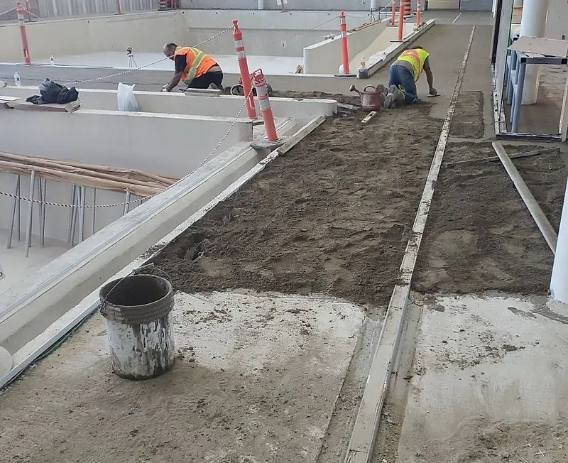 Two workers in hi-vis vests kneeling and floating mortar between rails along an indoor pool