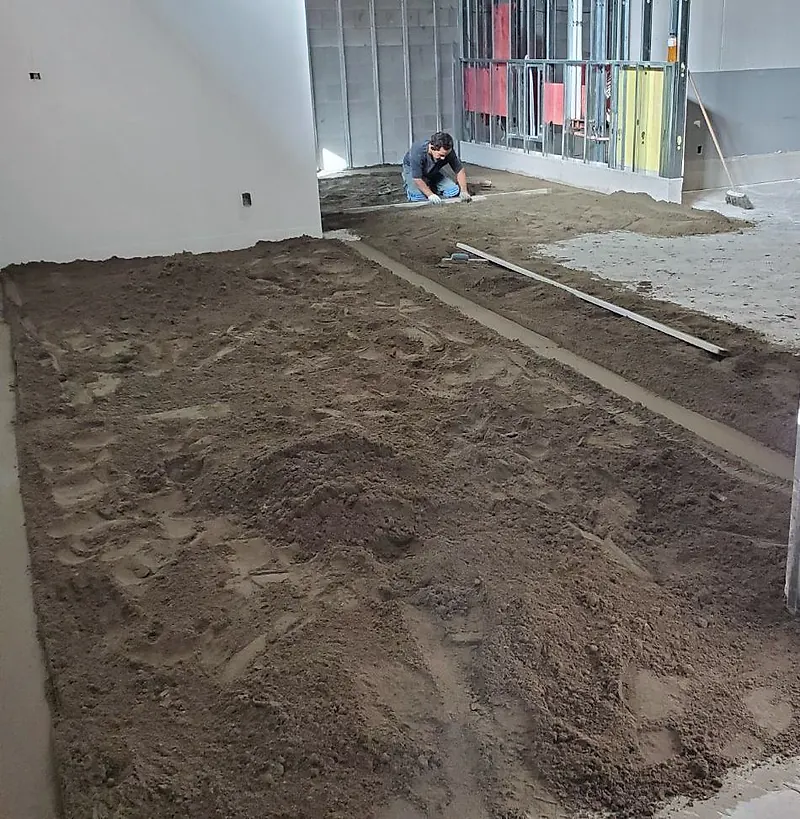 Large room with loose mortar spread in bays between screed strips, steel stud framing behind