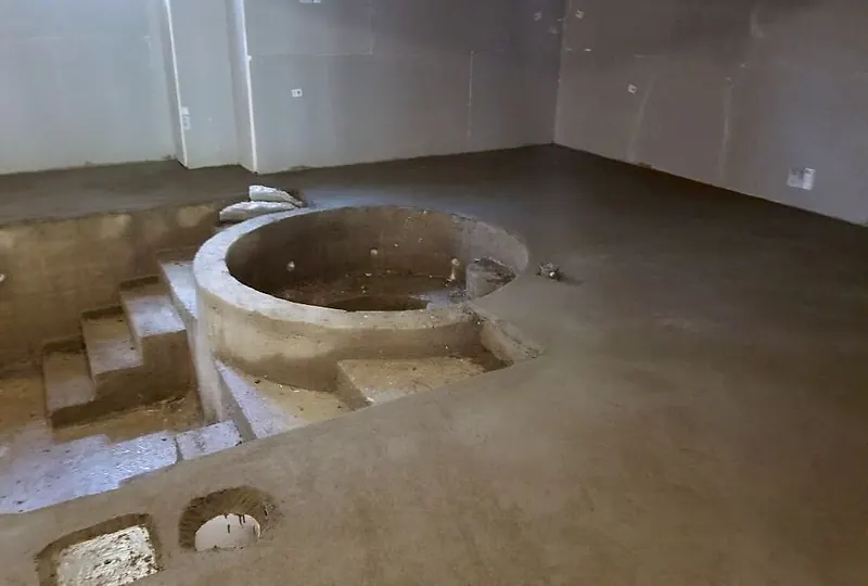 Mortar bed deck around a round concrete spa with steps, in a basement pool room