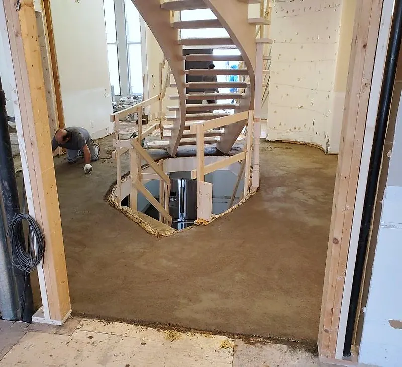 Fresh mortar bed around a curved staircase opening, a worker kneeling at the left