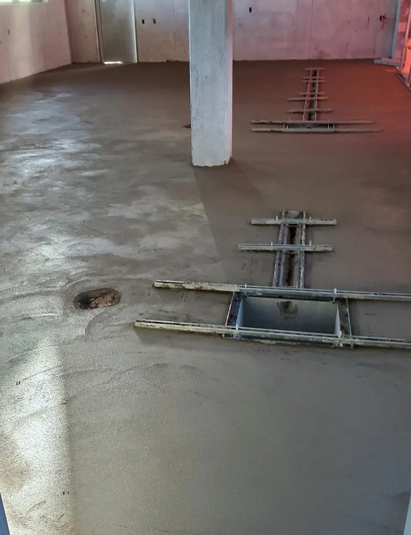 Freshly screeded floor in a concrete-walled room with steel screed rails around a rectangular trench opening