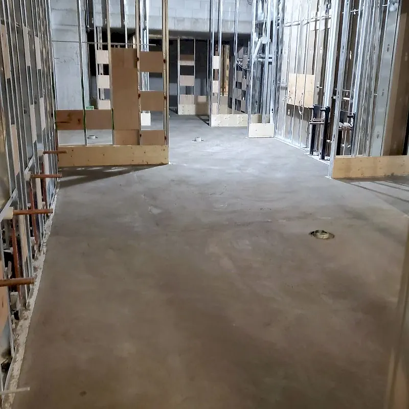 Finished mortar floor in a commercial corridor with steel stud partitions, copper plumbing stubs and a floor drain
