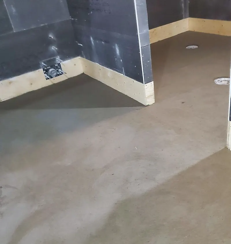 Finished mortar floor in a washroom compartment with cement-board walls and two drain flanges