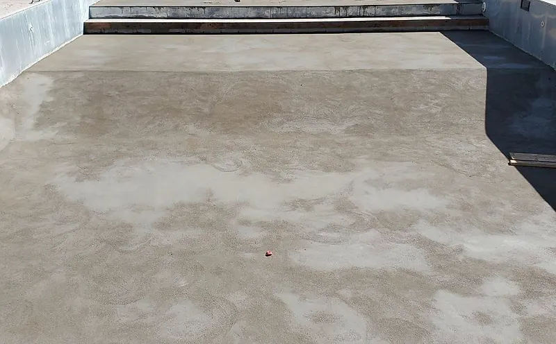 Floated mortar bed across the floor of an outdoor pool, one worker at the top step